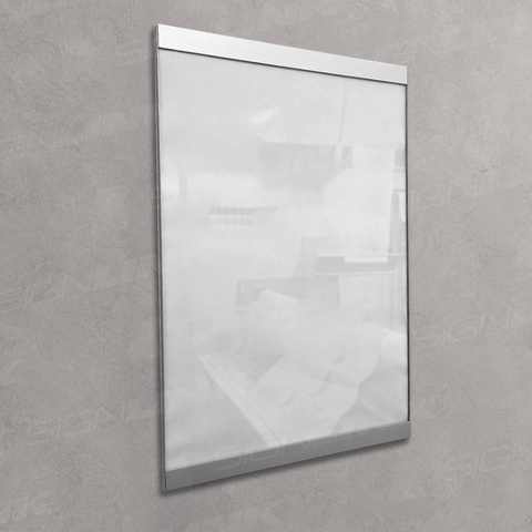 A vertical rectangular glass or acrylic display panel with a slim metallic frame, mounted on a textured gray wall. The panel is shown empty and slightly reflective, with faint interior room reflections visible.